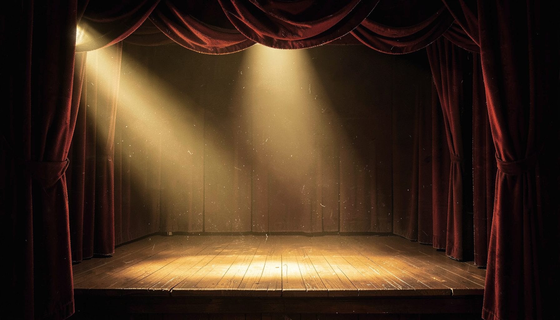 Warm stage lighting casting a golden glow across an empty wooden theater stage with heavy velvet drapes framing the proscenium arch